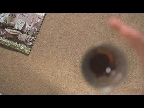Overhead view of a spilled liquid on beige carpet near a magazine.
