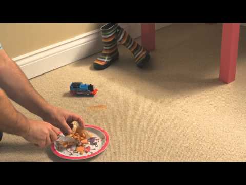 Person scraping spilled food off carpet next to a toy train.