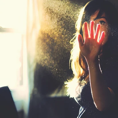 Woman raising her hand toward sunlight filtering through dust motes in the air.