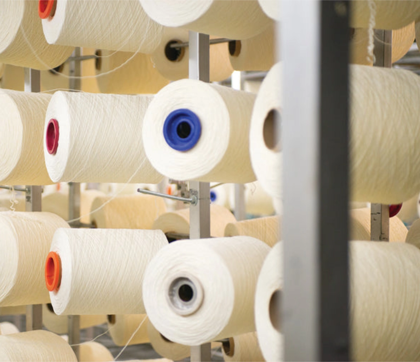 Spools of cream yarn arranged on factory shelving racks.