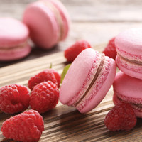 Pink macarons and fresh raspberries on a wooden surface.