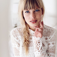 Portrait of a blonde woman in a white lace top resting her hand on her face.